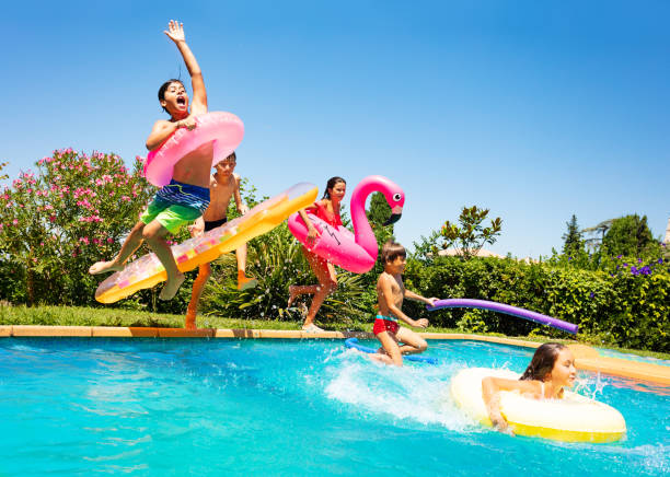 Happy friends jumping in pool on the vacations Group of age-diverse boys and girls, happy friends with swim floats jumping into swimming pool on the vacations foam rubber stock pictures, royalty-free photos & images