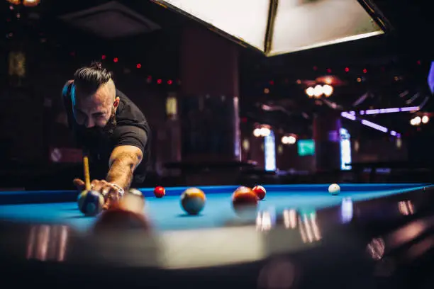 Young man with long beard playing snooker in a pub