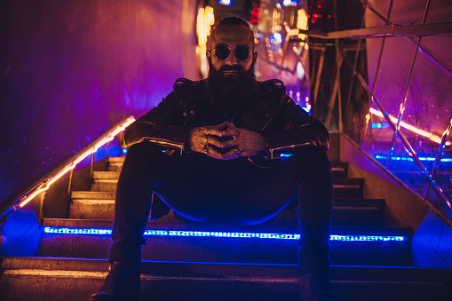 Biker with long beard sitting on stairs with neon lights
