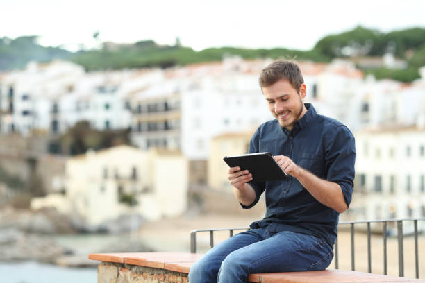 homem feliz usando um tablet em uma borda de férias - balcony beach book men - fotografias e filmes do acervo