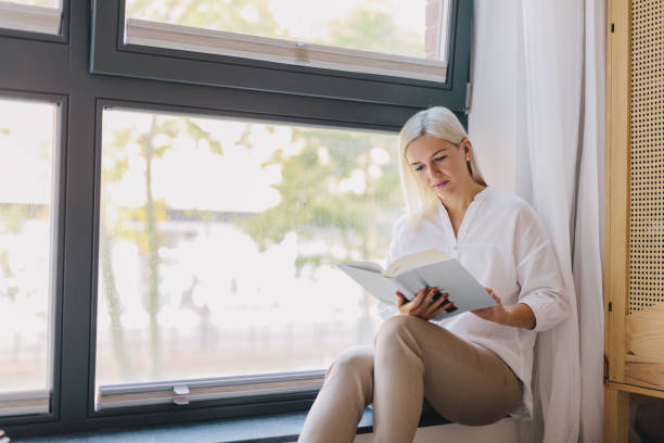 istock Woman reading book at home by the window. 1080330376