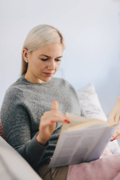 istock Woman reading book, sitting on the couch. 1080330396