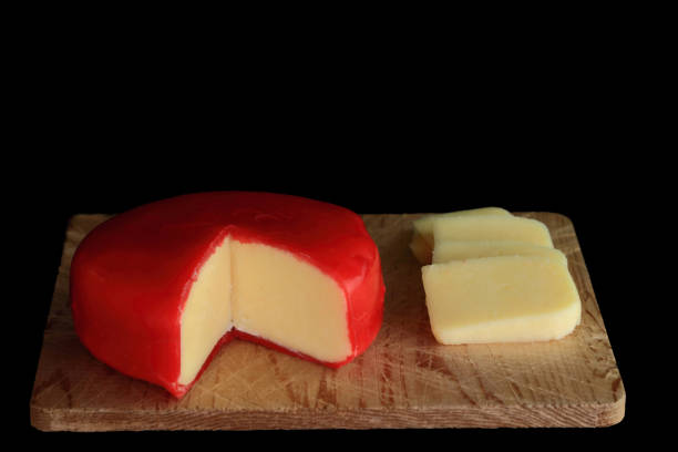 Wheel of Gouda Cheese and slices Wheel of Gouda Cheese with cut segment (wedge) and slices wheel of cheese is covered with red wax protective layer on wooden cutting board over black background gouda south holland stock pictures, royalty-free photos & images