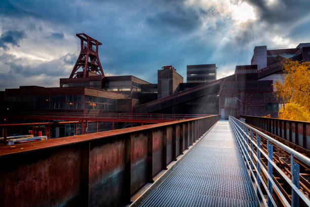 Industrial interior with a long metal walkway and overhead structures in a dimly lit factory setting.