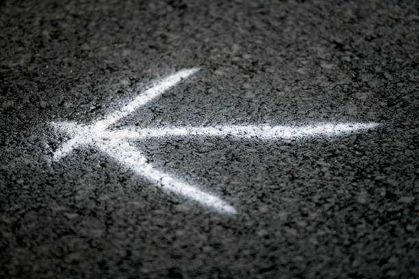 A white arrow has been spray painted on the black asphalt of walking, running and bicycling path the show the directions for runners during a local sports event for runners.