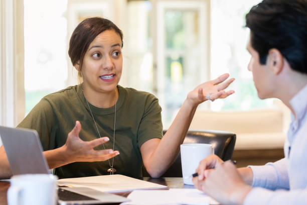 Woman in uniform gestures as she talks with a man Hispanic, adult woman gestures with her hands as she sits across from her husband at a table full of papers and a laptop. She is wearing army clothing. proud army mom stock pictures, royalty-free photos & images