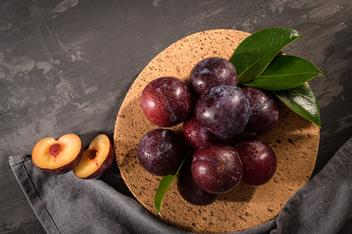 Delicious red plums in a cork plate on kitchen countertop.