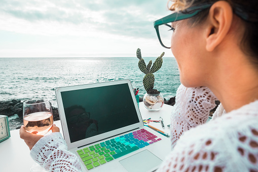 free digital nomad woman at work with a laptop sitting in front of the ocean in free outdoor space like alternative kind of closed office. Working with technology in nature place with freedom for people