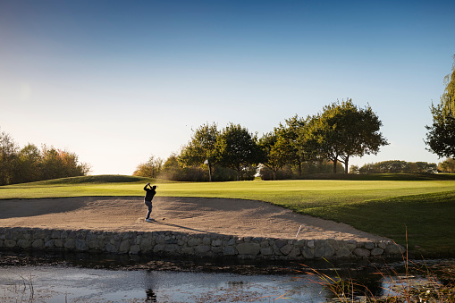 Portrait of a golfer as he hits a perfect bunker shot out of the sand. Photographed in the late autumn sunlight  on a course on the island of Møn in Denmark. Colour, horizontal with some copy space.