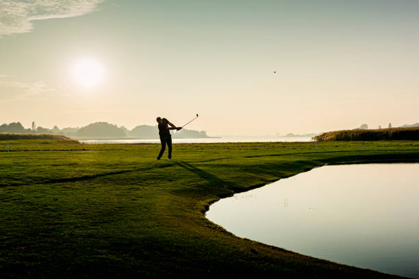 Hitting the perfect pitch shot. Golfer hitting a delicate wedge shot over a water feature and towards the flag. Photographed in the late autumn light on a course on the island of Møn in Denmark. Colour, horizontal with some copy space. golf concentration stock pictures, royalty-free photos & images