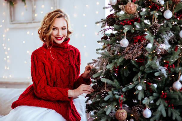 uśmiechnięta kobieta w czerwonym swetrze na tle choinki - christmas women human lips female zdjęcia i obrazy z banku zdjęć