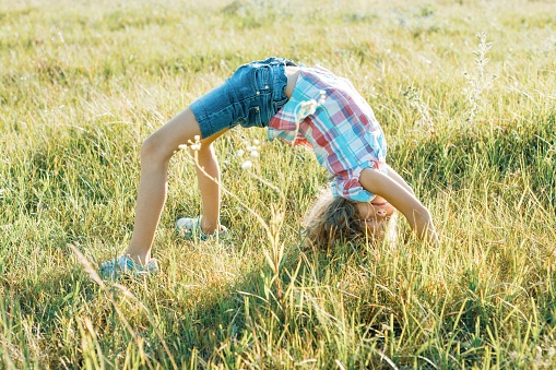 Happy little athletic girl child doing an acrobatic handstand on nature in summer park.