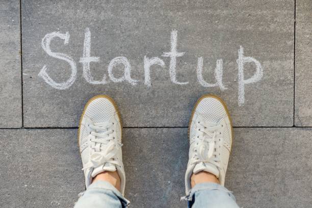 istock View from above, female feet with text startup written on grey sidewalk 1080380136