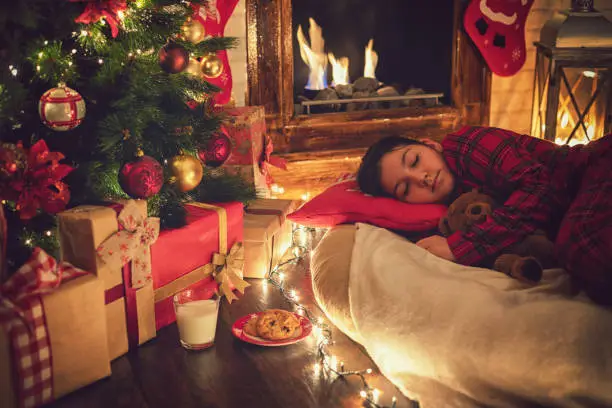 Photo of Little girl in pajama fell asleep near tree on Christmas Eve