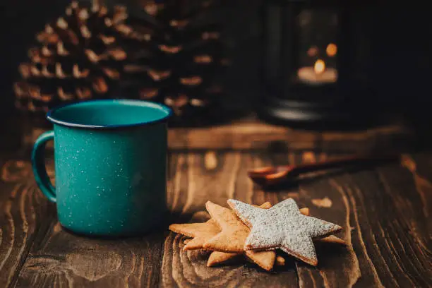 Photo of Enamel cup with hot chocolate and star shaped cookies, wood cabin, winter nights
