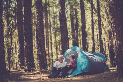 Couple of senior adult people caucasian do freedom camping in a forest under high pines together with a tent in wild alternative travel vacation to live and enjoy the nature and the world around. Happy couple in forest