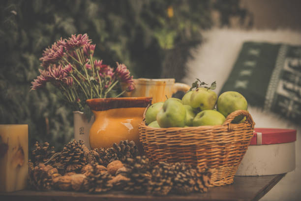 Green apples in a basket, pine cones, walnuts, and flowers in a vase are arranged on table in back yard.