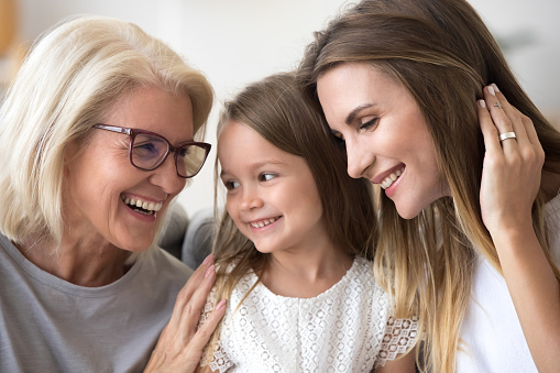 Smiling loving three generation of women concept laughing, grandmother, daughter and child girl bonding together, happy senior old grandma embracing kid granddaughter and grown mom having fun at home