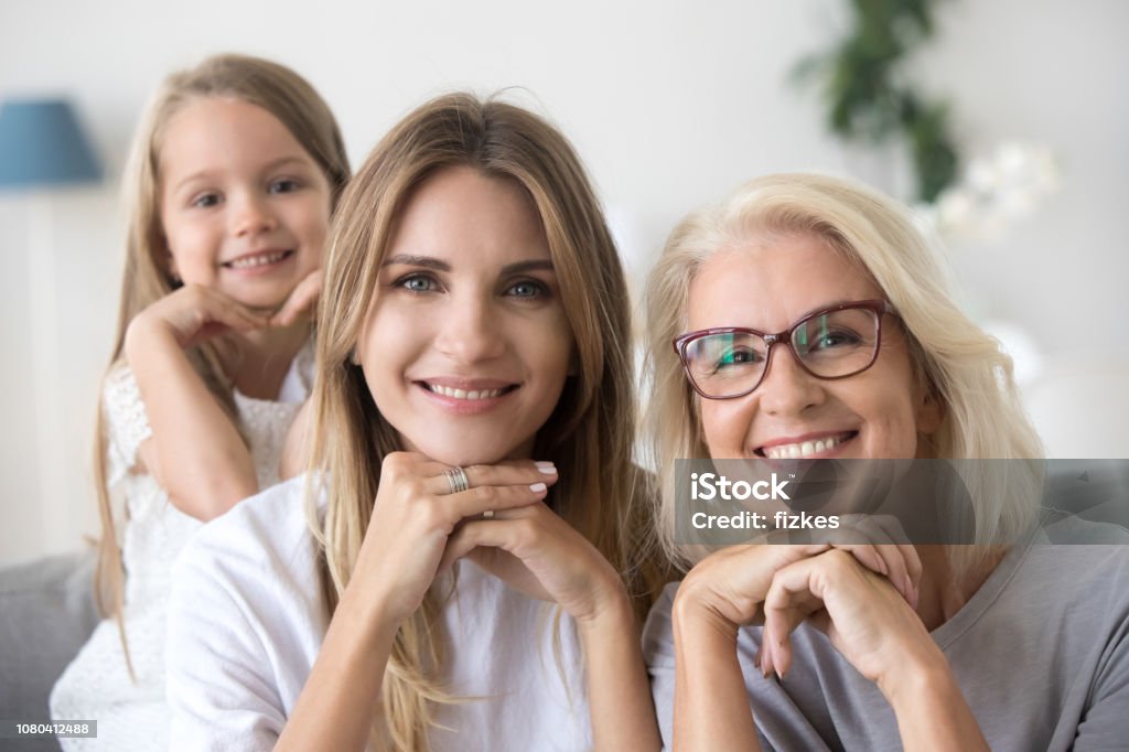 Portrait of happy three women generation grandma mom and child Portrait of happy three women generation, grandma mom and child granddaughter holding hands under chin looking at camera, young smiling adult daughter, older grandmother and kid girl family headshot Women Stock Photo