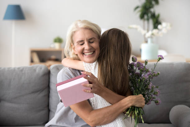 happy senior grandma hugging granddaughter thanking for gift and flowers - grandmother giving gift child imagens e fotografias de stock