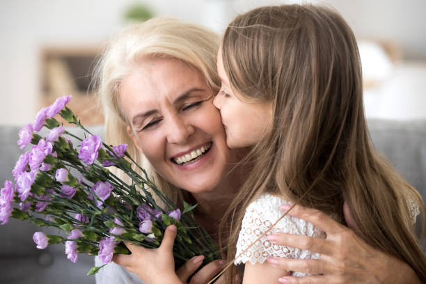 piccola nipote che si bacia dando bouquet di fiori congratulandosi con la vecchia nonna sorridente - grandmother giving gift child foto e immagini stock