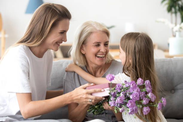 szczęśliwa babcia dziękując wnukowi i dorosłej córce za prezenty z kwiatami - grandmother giving gift child zdjęcia i obrazy z banku zdjęć