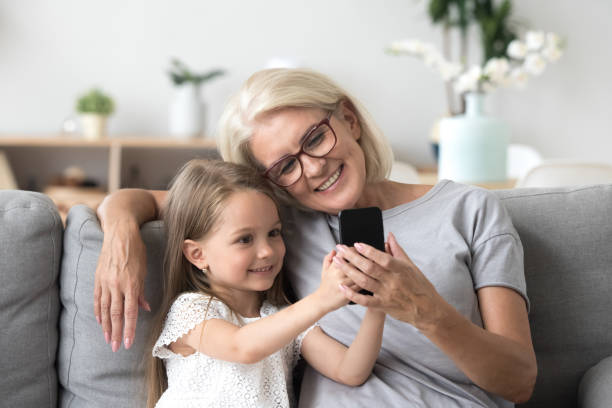 nonna felice e nipote carina che usa il cellulare facendo selfie insieme - grandparent family multi generation family technology foto e immagini stock