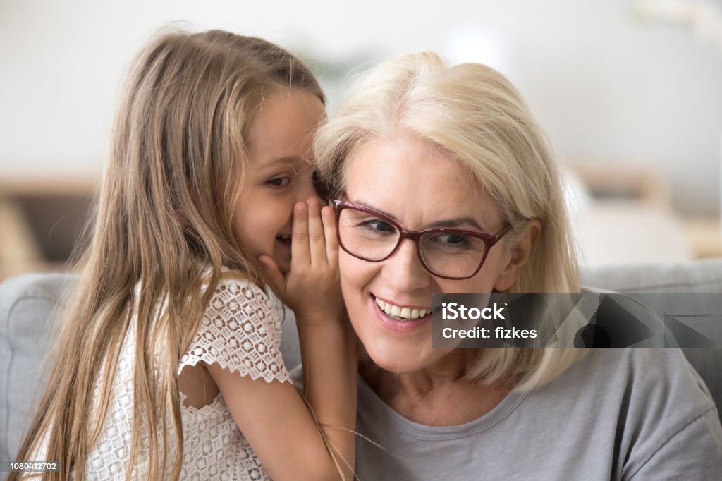 Petite-fille de petit mignonne chuchoter à l’oreille en disant secret de grand-mère - Photo de Enfant libre de droits