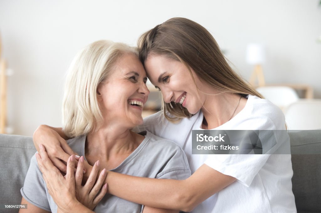 Happy loving older mother and grown millennial daughter laughing embracing Happy loving older mature mother and grown millennial daughter laughing embracing, caring smiling young woman embracing happy senior middle aged mom having fun at home spending time together Mother Stock Photo