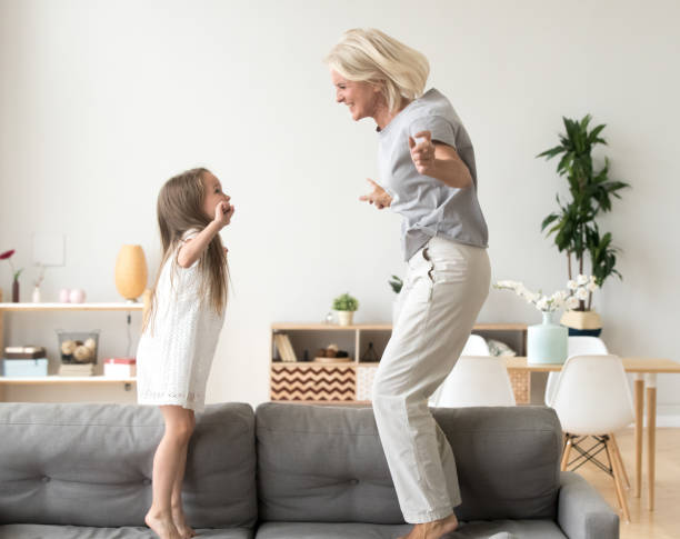 cute little girl playing with grandmother jumping on couch together - grandmother action senior adult grandparent imagens e fotografias de stock