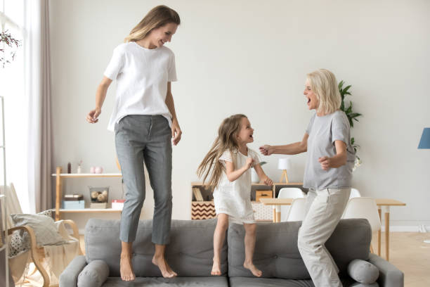 happy kid, mother and grandmother having fun jumping on sofa - grandmother action senior adult grandparent imagens e fotografias de stock