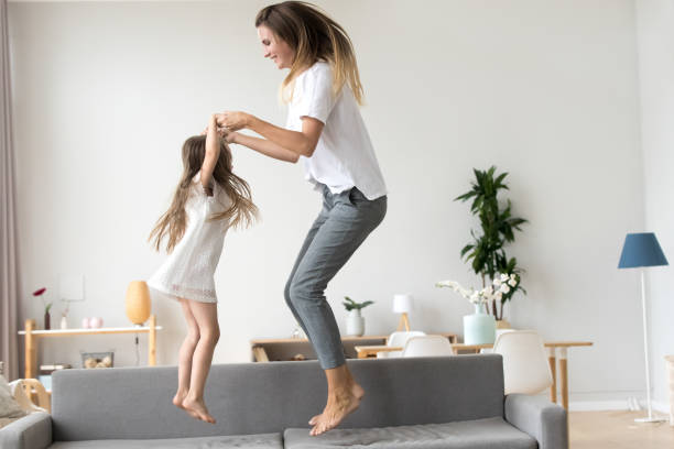 istock Happy mommy and kid daughter holding hands jumping on sofa 1080412902
