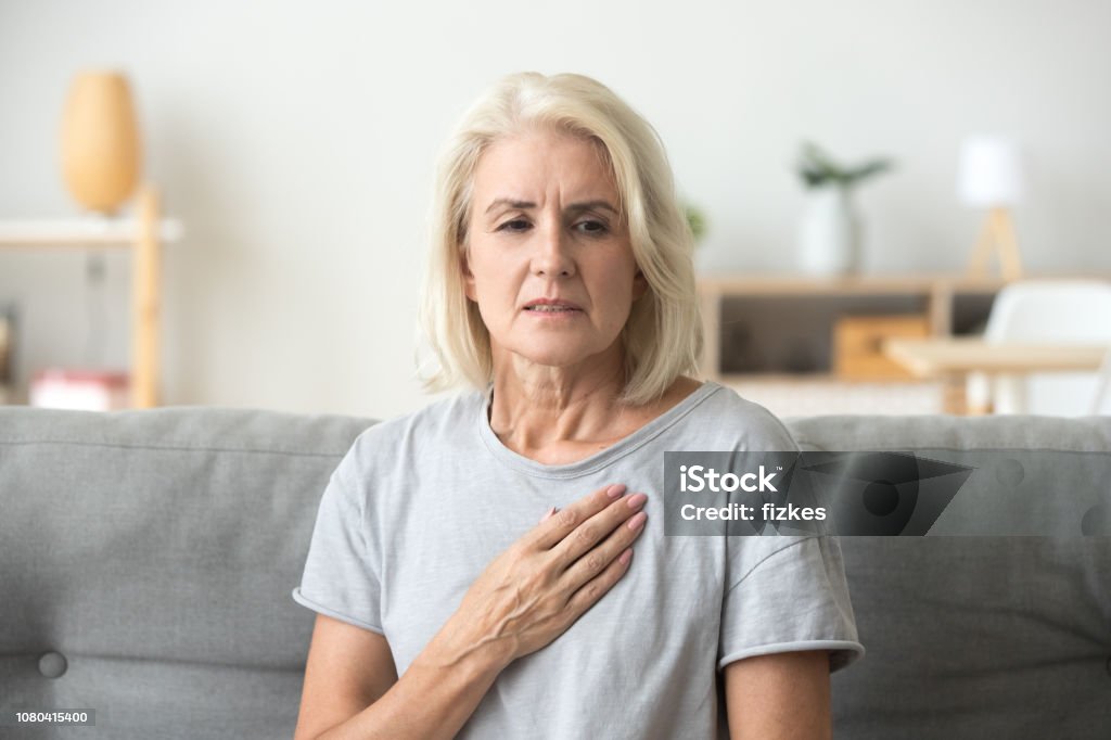 Upset stressed mature older woman feeling heartache touching chest Upset stressed mature middle aged woman feeling pain ache touching chest having heart attack, sad worried senior older lady suffers from heartache at home, infarction or female heart disease concept Heart - Internal Organ Stock Photo