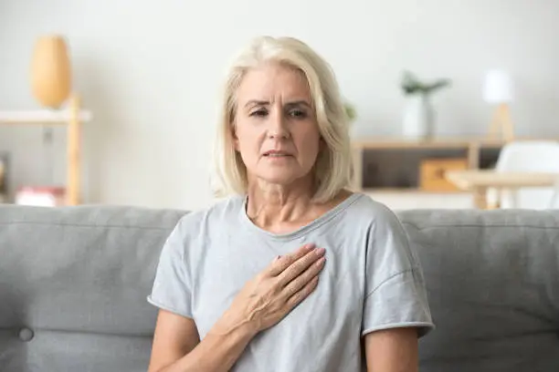 Upset stressed mature middle aged woman feeling pain ache touching chest having heart attack, sad worried senior older lady suffers from heartache at home, infarction or female heart disease concept