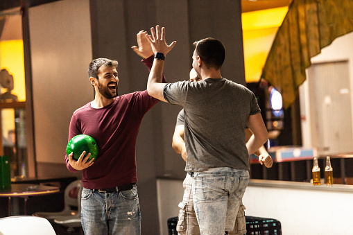 Three men are high fiving and celebrating their score in bowling.