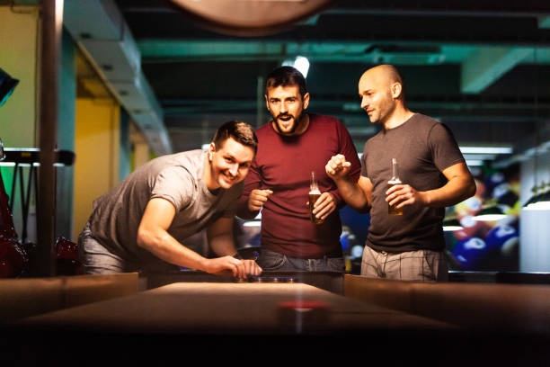 freunde spielen shuffleboard in schwimmhalle - pool game pool table aiming men stock-fotos und bilder