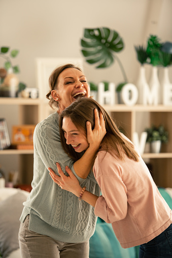 Mother and her teenage daughter laughing and enjoying together while they dance in the living room.