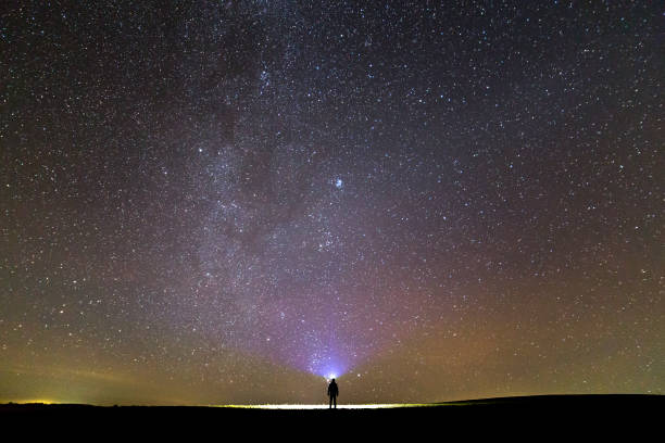 istock Black silhouette of man with head flashlight on grassy field under beautiful dark summer starry sky. 1080445324
