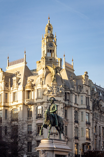 Vertical shot of the D. Pedro IV Statue in Avenida dos Aliados, in Porto, Portugal, against gothic architecture buildings, on a clear blue day.