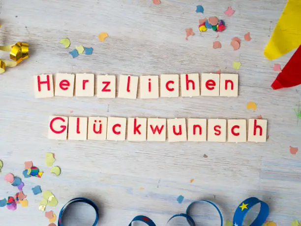 Herzlichen Glückwunsch (congratulations) lettering with party supplies on wooden background, concept image