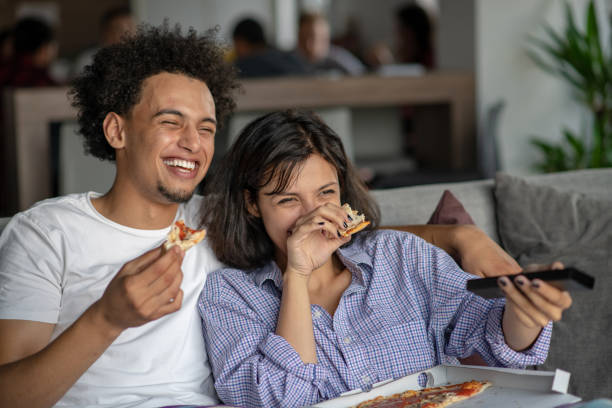 pareja feliz viendo la televisión mientras comen pizza. profundidad de campo, foco en el hombre - apartment television family couple fotografías e imágenes de stock