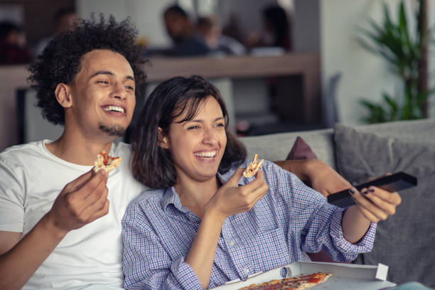 pareja feliz viendo la televisión mientras comen pizza. profundidad de campo, foco en el hombre - apartment television family couple fotografías e imágenes de stock