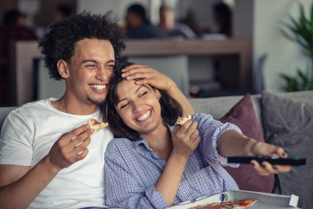 幸せなカップルは、ピザを食べながらテレビを見ています。男に焦点を当てる、フィールドの浅い深さ - apartment television family couple ストックフォトと画像