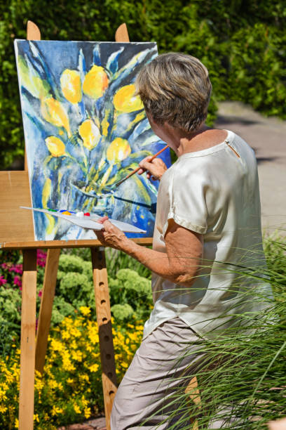 Senior mujer pintura en caballete en jardín. - foto de stock