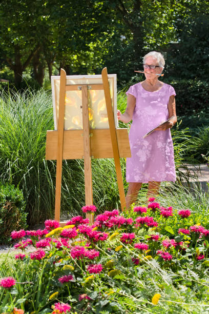 Senior mujer pintura en jardín en día soleado. - foto de stock