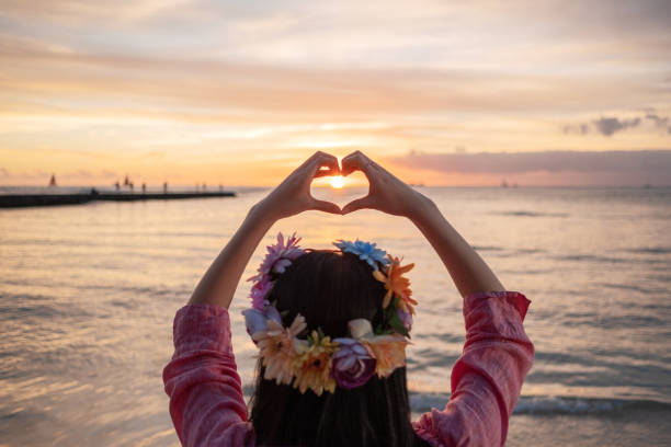 Woman with flower head crown making heart sharp with hands