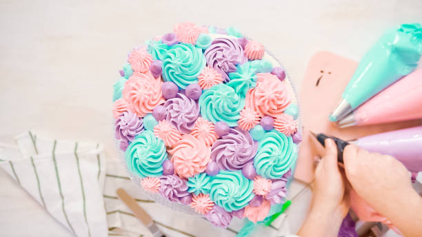 Flat lay. Piping pastel color buttercream rosettes on a white cake to make a unicorn cake.