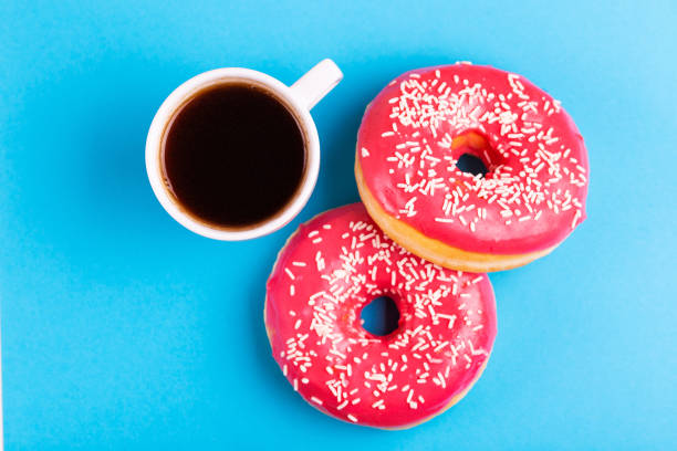 istock Two delicious pink donuts with sprinkle and cup of coffee on bright blue background 1080619630