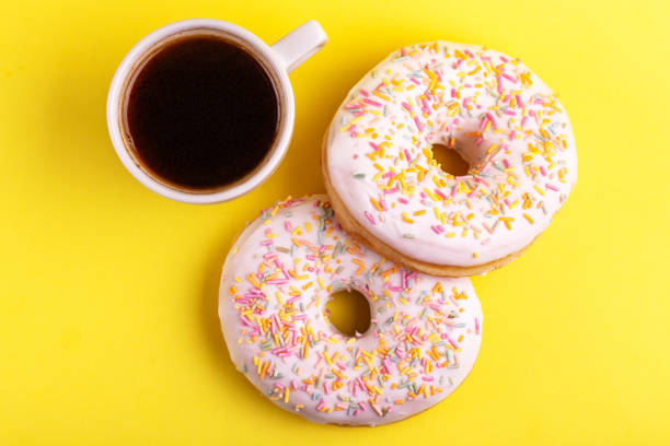 istock Two delicious vanilla donuts with sprinkle and cup of coffee on bright yellow background 1080619782