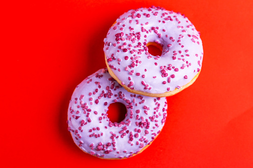 Two delicious lilac donuts with sprinkle on bright red background. Unhealthy, but tasty sweets. Copy space. Top view